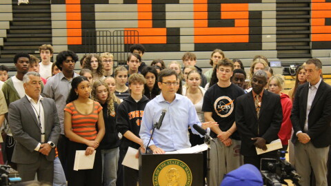 Gov. Bob Ferguson stands with students, teachers and administrators in front of a podium, inside the Lewis & Clark gymnasium. 