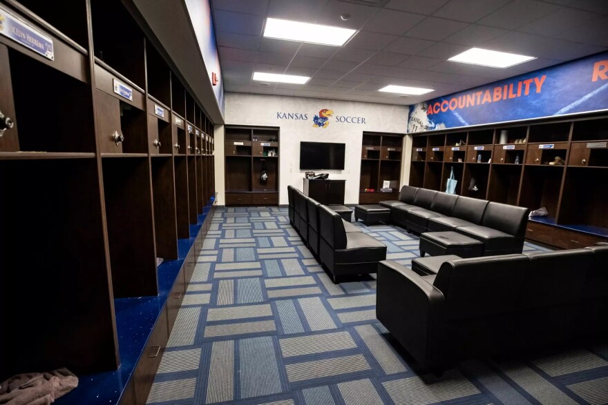 A college sports locker room lined with open-faced lockers and couches in the middle of the room