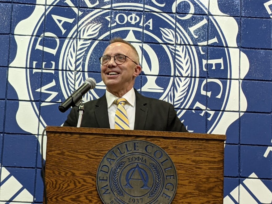 Medaille College President Kenneth Macur stands at a Medaille College podium, with the Medaille College logo on the wall behind him