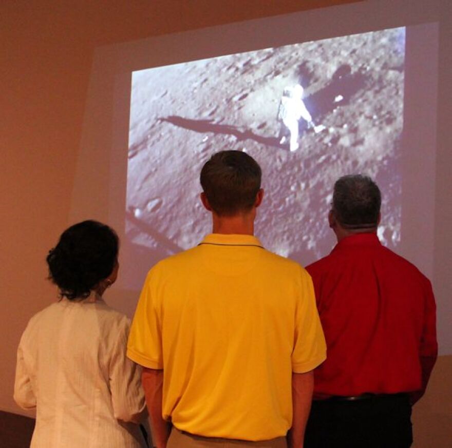 Three guests watch video of Apollo lunar landing during 2014 Moon Museum exhibition at Bob Rauschenberg Gallery