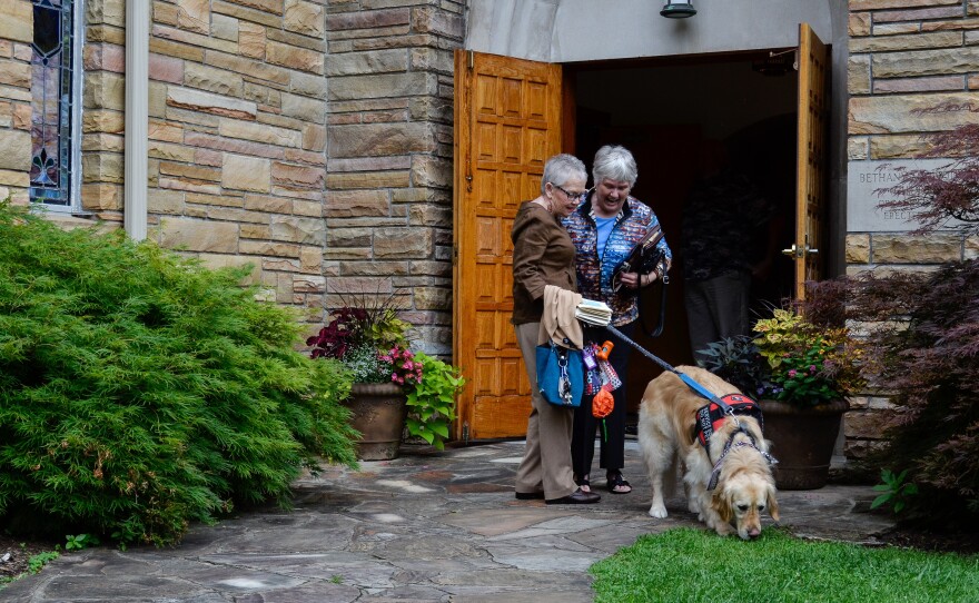 Peggy Gibson (left) guides her diabetic alert dog Rocky outside as she talks with a friend following a church service at Bethany United Methodist Church in West Jefferson, N.C., on July 7, 2019. The congregation helped Gibson raise the money to purchase Rocky.