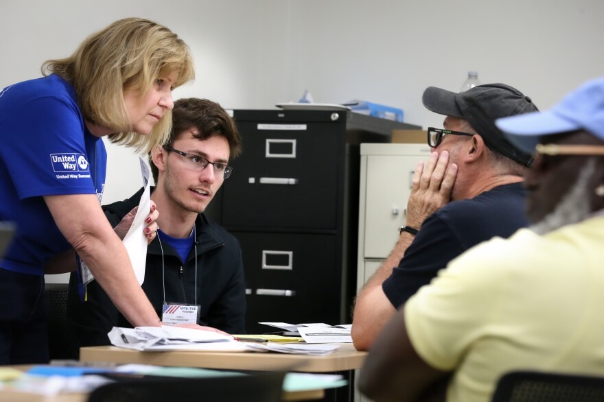 A man receives financial assistance at United Way Suncoast's VITA Tax-A-Thon in February 2025. He has his hands up to his face and sits across from a young man and a woman who is leaning over the table.