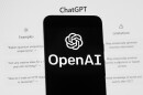 The OpenAI logo is seen on a mobile phone in front of a computer screen which displays the ChatGPT home Screen, Friday, March 17, 2023, in Boston.