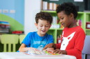 Student in international preschool reading a magazine book together in school library, education, kid and study concept