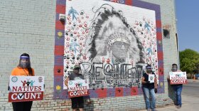 FILE - Activists hold signs promoting Native American participation in the U.S. census in front of a mural of Crow Tribe historian and Presidential Medal of Freedom recipient Joe Medicine Crow on the Crow Indian Reservation, Aug. 26, 2020, in Lodge Grass, Mont. A majority of tribal groups won't get the full suite of detailed demographic data from the 2020 census that they had in the previous census. Some of the available numbers are going to be imprecise because of new privacy safeguards recently implemented by the U.S. Census Bureau, according to a new report by the Center for Indian Country Development. (AP Photo/Matthew Brown, File)
