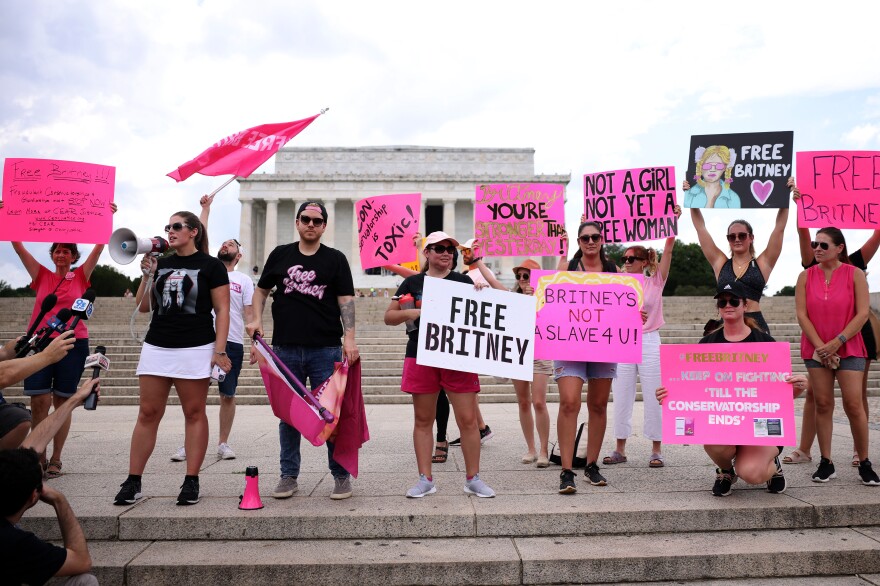 Several people stand on the steps of the Lincoln Memorial holding megaphones and pink signs with slogans including "Britney's Not A Slave 4 U!" and "Free Britney."
