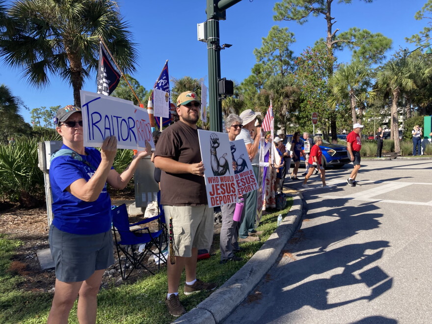Demonstrators wave signs as people walked to Alico Arena to see and hear President Trump. Protestors shouted at Trump supporters, asking them about the Iran war, gas prices and the Jeffrey Epstein files.