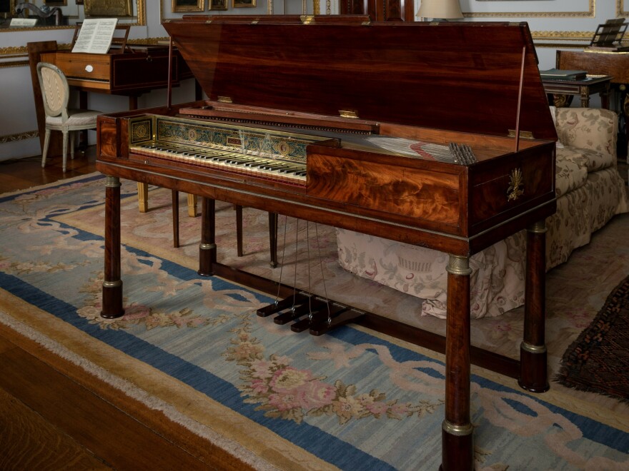 The piano is a so-called square model that is more like a rectangular box on legs. The body is made out of mahogany and decorated with bronzes and verre églomisé, or reverse-painted and gilded glass.