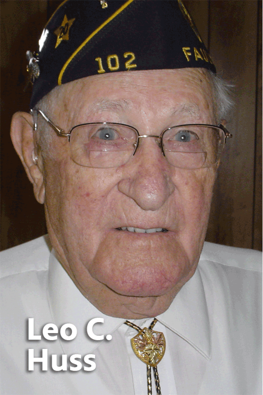Elderly Leo Huss wearing glasses, a white button-up shirt and bolo tie, and a navy blue veteran's cap.