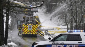 Police block a road as a firefighter works on a water line at a house fire, Thursday, April 4, 2024, in Derry, N.H. Derry Fire Chief Shawn Haggart said his department received reports of an explosion and responded to find a house fully engulfed in flames. (AP Photo/Charles Krupa)