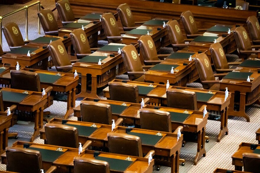 a closeup view of empy chairs and desks in the state house chamber