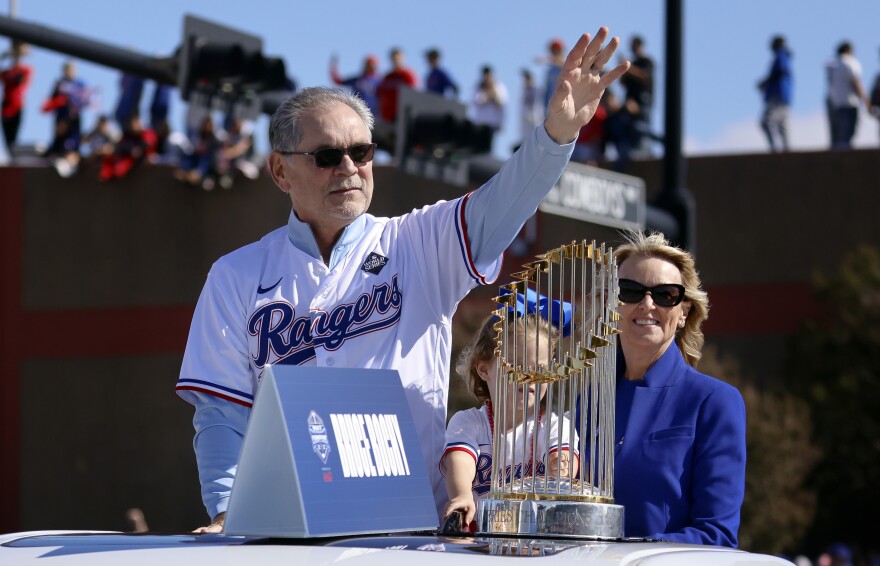 Riding with the Commissioner's Trophy, Texas Rangers manager Bruce Bochy, left, waves to fans as his wife Kim Seib, right, looks on during a parade for the baseball World Series-champion team in Arlington.