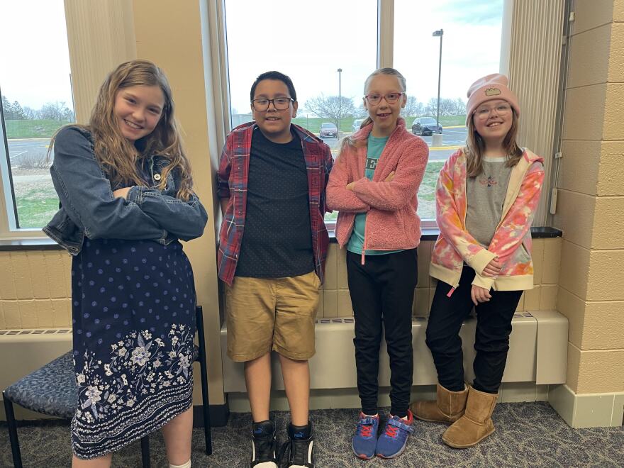 Student reporters Hannah, Annika,  Edgar, and Ellie stand in front of a window after recording their phenology report. 