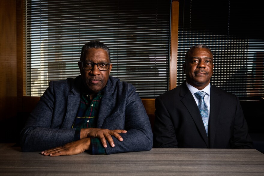 CapMetro Executive Vice President Gardner Tabon and the agency's soon-to-be police chief, Eric Robins, sit for a portrait inside a conference room. Both are in suits facing the camera. Behind them are window blinds through which you can make out some of Austin's downtown skyscrapers.