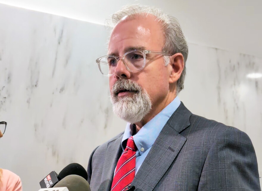 A man in a suit talks into microphones.