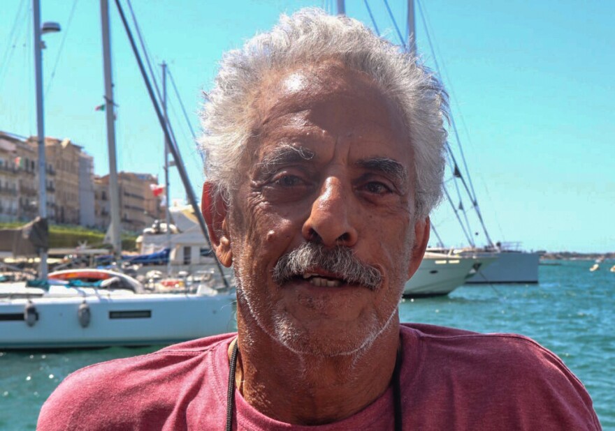 Bob Suberi stares directly at the camera. Boats and water visible behind him.