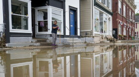 Kathy Eason, a worker at the Center for Highland Falls, stands outside the organization's storefront after being trapped inside by floodwaters the previous day, Monday, July 10, 2023, in Highland Falls, N.Y. Heavy rain has washed out roads and forced evacuations in the Northeast as more downpours were forecast throughout the day. One person in New York's Hudson Valley has drowned as she was trying to leave her home. (AP Photo/John Minchillo)
