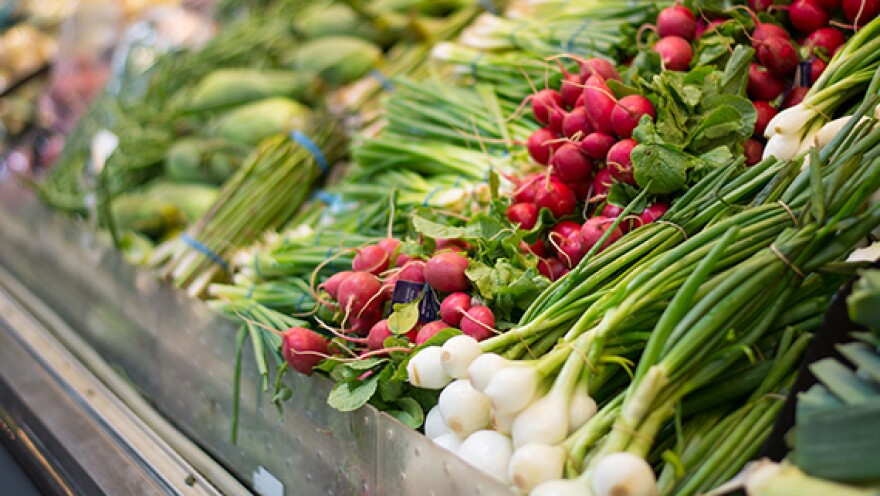 Grocery store vegetable shelf with spring onions, radishes and other produce