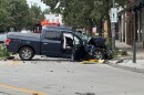 A damaged pickup truck sits on a city street in a small downtown area