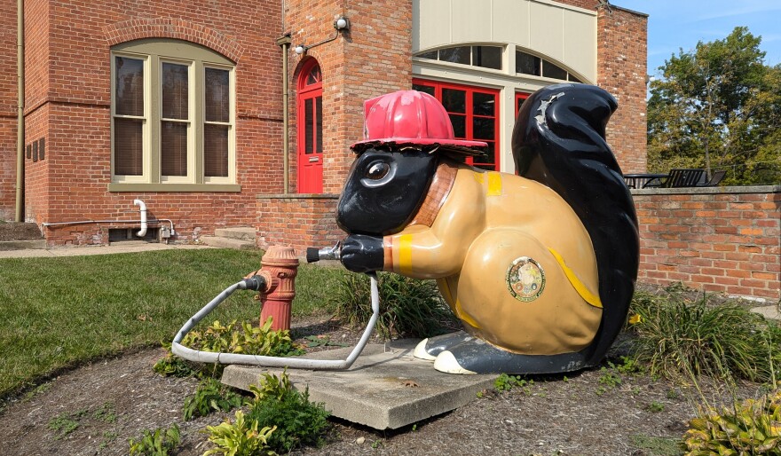 A fiberglass statue of a black squirrel dressed as a firefighter.