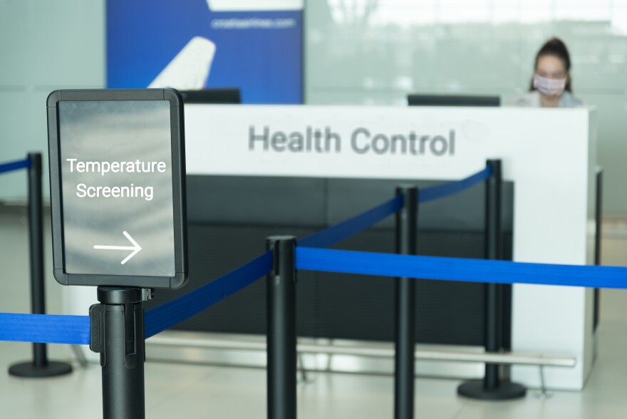 Temperature screening sign at an airport with a woman wearing a mask sitting at health control counter.