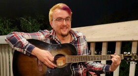 A man plays guitar and smiles for camera