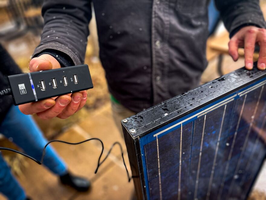 Richard Stromberg, a professor at Western Colorado University and co-founder of Equitable Solar Solutions, holds up a USB port that can charge a phone by the power of the sun.