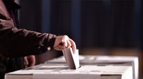 A hand dropping a ballot in a box. 