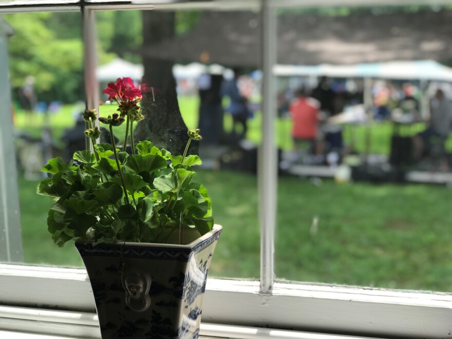 A potted flower sits in a window of the Happy Retreat mansion. Outside is the back lawn of the house. A temporary stage has been built for the Wine and Jazz Festival on June 9, 2018.