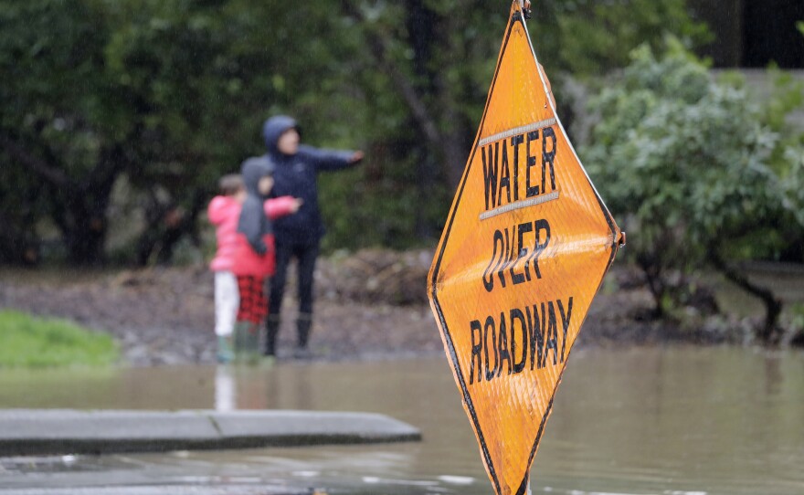 Pedestrians look at the flood waters of Issaquah Creek Thursday, Feb. 6, 2020, in Issaquah, Wash. Heavy rain sent the creek over a major roadway, under an apartment building and up to the foundations of homes as heavy rains pounded the region.