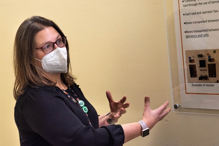 A woman wearing a face mask gestures at an informational display.