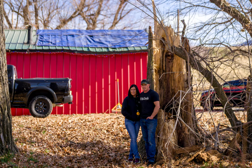Owners of a Logan coffee shop stand beside the trunk of a massive fallen tree that crushed the roof of their red roastery behind them.