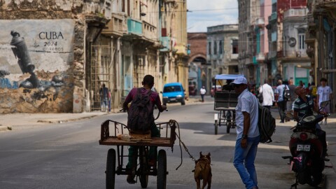 A man rides a tricycle with his leashed dog running alongside him during a blackout in Havana, Cuba, Monday, March 16, 2026. 