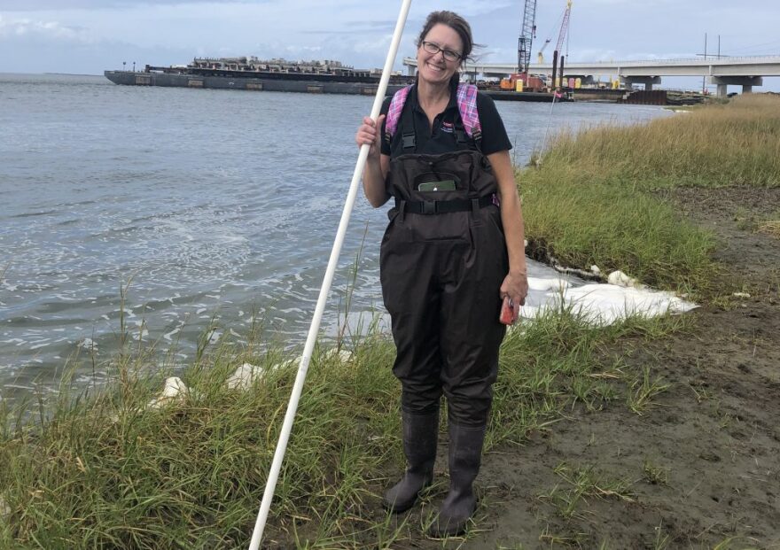 Woman in waders standing on a shore and holding a pole