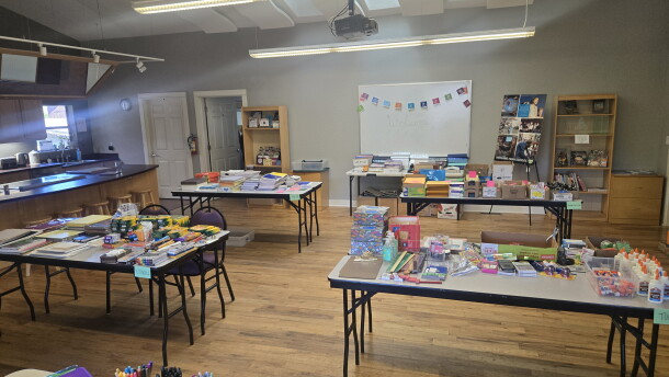 White folding tables are lined up in rows, covered with markers, paper, and other colorful school supplies. 