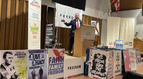A man stands at a podium surrounded by signs that say phrases including "freedom" and "team America"