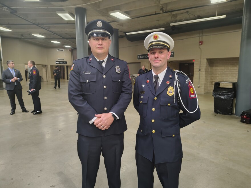 Two men in firefighter attire pose for a photo