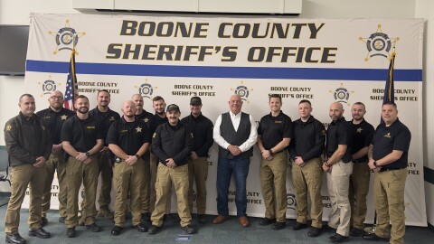 Men in black shirts and khakis pose in front of Boone County banner