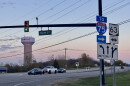 Cars sit stopped at a red light with a sunset and Monroe water tower in the background.