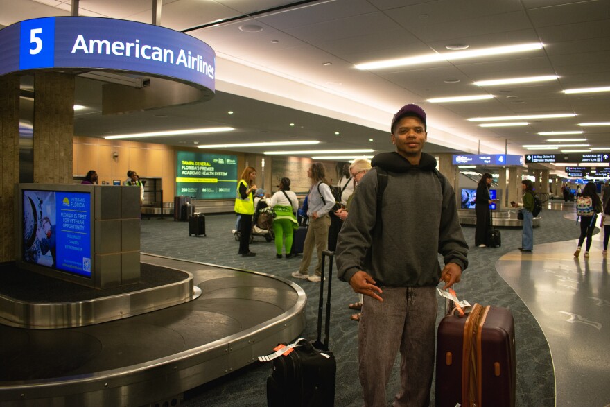 A man stands with his luggage in baggage claim at Tampa's airport. 