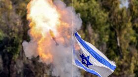 A mortar round flies past an Israeli flag waving atop an Israeli armoured vehicle from a position along the border in southern Israel amid the ongoing conflict between Israel and the Palestinian militant group Hamas.
