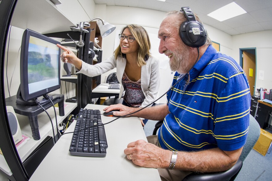 An elderly man sits at a computer with headphones on doing Cognitive Brain Training.