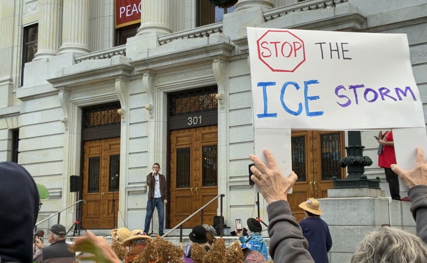 David Smith speaks to the crowd holding signs including one that says "Stop the ICE storm" 