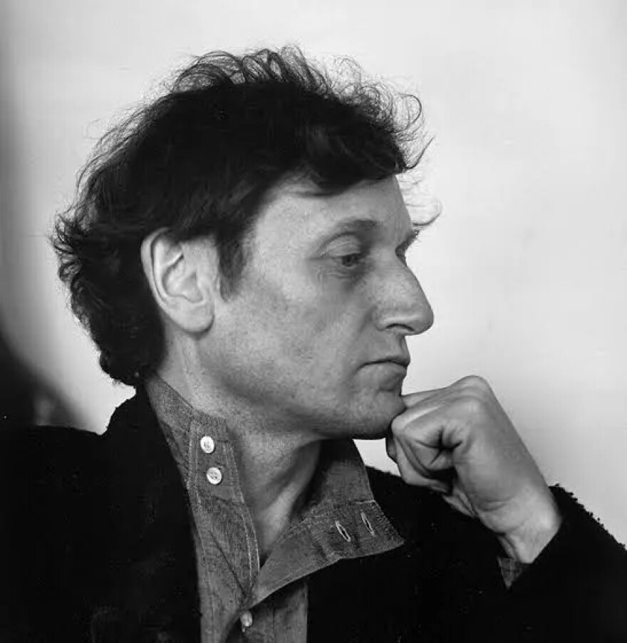 Composer Gérard Grisey faces towards the right, fist on chin, expression slightly lowered and hair messy. He appears to be wearing a sort of buttoned shirt underneath a sports coat. The photo is black and white.