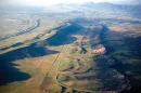 A bird's-eye view overlooks rolling green hills. A network of residential road snakes its way across the foothillls of a mountain range.