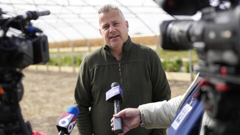 U.S. Rep. Eric Sorensen talks to media on a farm while wearing a forest green quarter-zip sweater