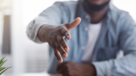 a man sitting behind a desk extends his hand for a handshake 