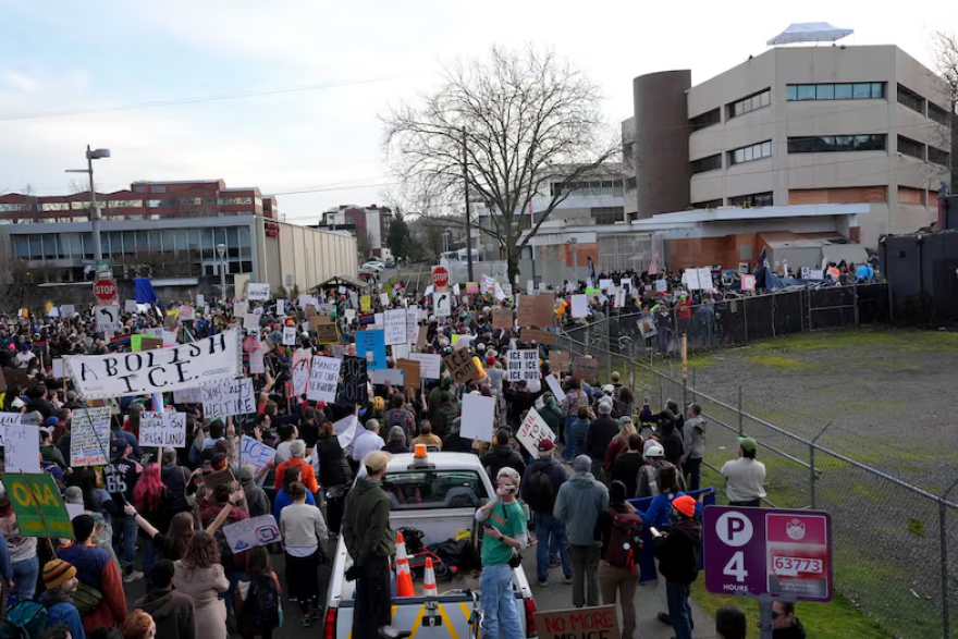 A crowd of people with signs stand along a fenced area.