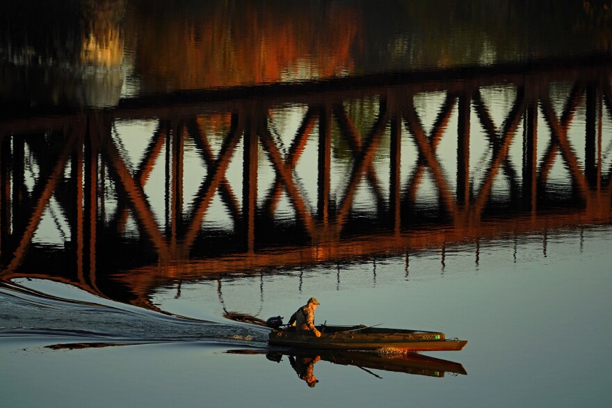 A duck hunter motors by the reflection of a train trestle on the Androscoggin River, Friday, Oct. 29, 2021, in Brunswick, Maine.