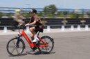 A boy in a baseball cap riding a bright red Bikabahn e-bike on a paved path.